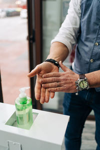Crop anonymous male barber in wristwatch applying antibacterial gel on hands at work in beauty salon