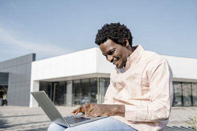 Smiling young businessman using laptop sitting on bench