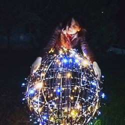 Woman standing by illuminated christmas lights at night