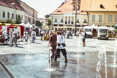 People on wet street against buildings in city