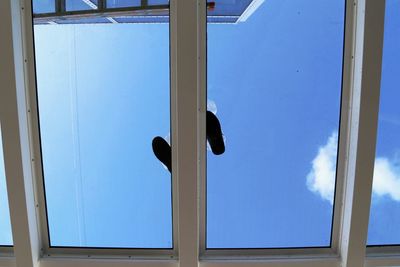 Low angle view of men standing on glass ceiling against blue sky