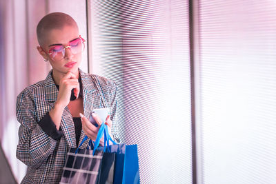 Low angle view of lesbian woman using smart phone holding shopping bags standing against abstract backgrounds