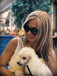 Smiling woman wearing sunglasses carrying dog in city