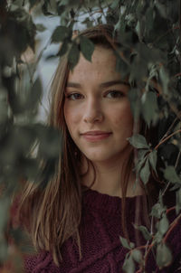 Portrait of beautiful young woman looking through plants outdoors