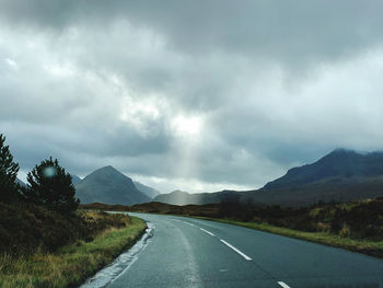 Empty road along landscape against cloudy sky