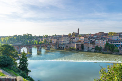 Bridge over river by buildings in city against sky