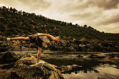 Side view of man standing on rock against sky