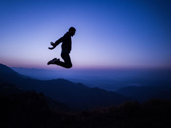 Silhouette man jumping in mountains against sky