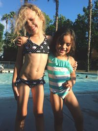 Sisters in swimsuit standing with arm around at poolside