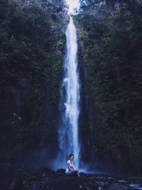 Woman sitting against waterfall in forest