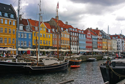 Sailboats moored on canal amidst buildings in city against sky