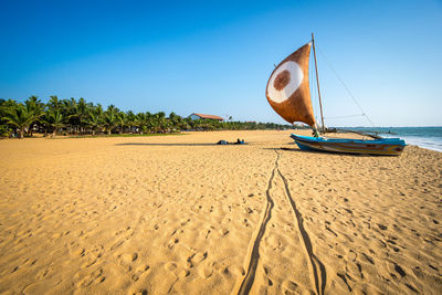 Sailboat moored on shore at beach against blue sky