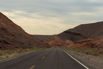 Empty road by mountains against sky