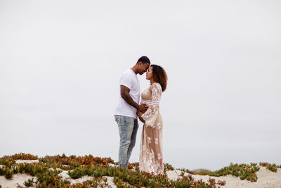 Mixed race couple embracing on sand dunes maternity
