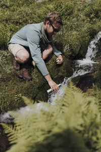 Full length of man filling bottle from waterfall