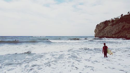 Rear view of man standing on beach against sky