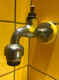 Close-up of faucet on yellow tiled wall