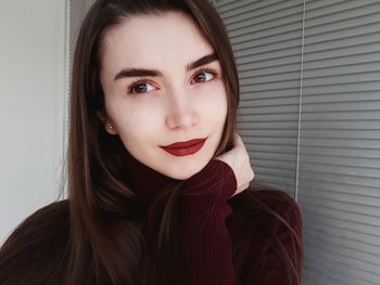 Close-up of beautiful woman with hand on chin by window blinds