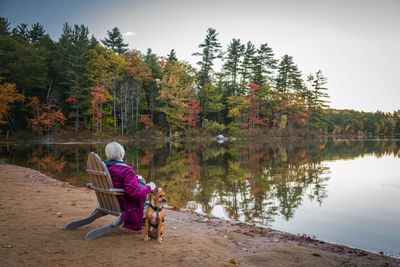 Woman with dog sitting by lake on chair during autumn