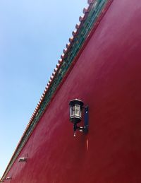 Low angle view of lamp on red wall against clear sky