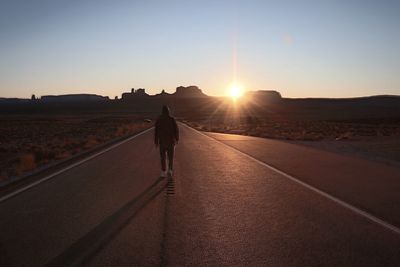 Rear view of man walking on road against sky during sunset