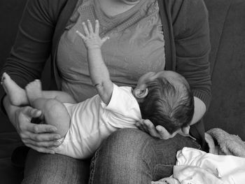 Midsection of father holding baby sitting at home