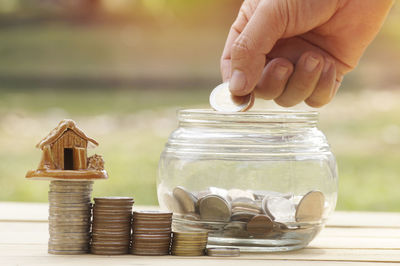 Close-up of hand putting coin in jar on table