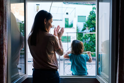 Mother and daughter applauding from the window of the house very happily