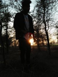 Man standing by tree in forest during sunset