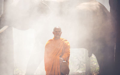 Monk standing by elephant at forest
