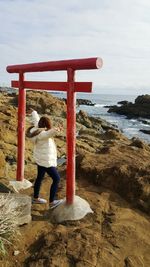 Full length of young woman standing by torii gate at beach