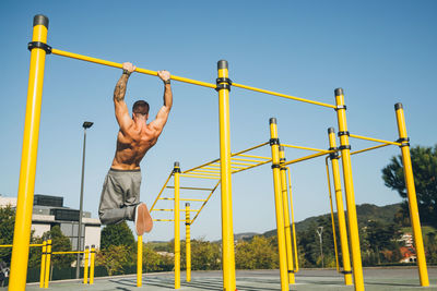 Rear view of man hanging on bar against sky