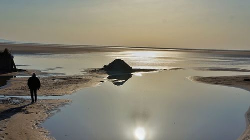 Rear view of people on beach against sky during sunset