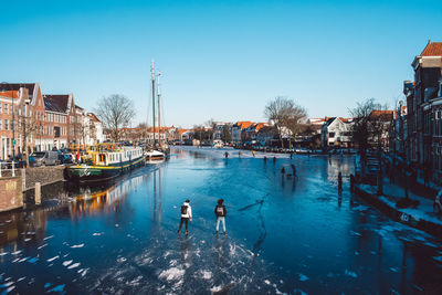 People on canal in city against clear blue sky