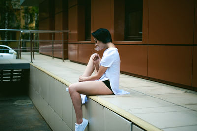 Full length of young woman sitting on walkway against orange building