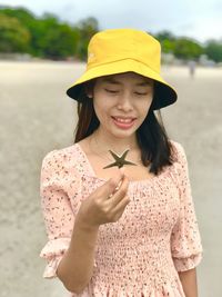 Woman wearing hat holding starfish standing at beach