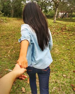 Cropped hand of man holding woman walking on field