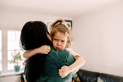 Rear view of mother carrying sad daughter while standing at home