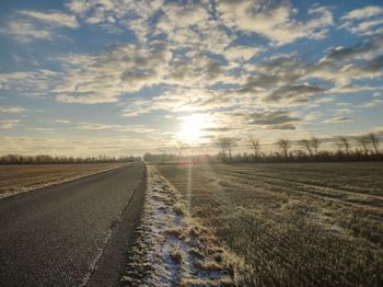 Empty road amidst field against sky during sunset