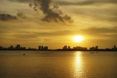 Silhouette buildings by sea against sky during sunset