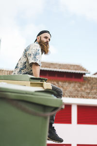 Male hipster tourist sitting on garbage bin