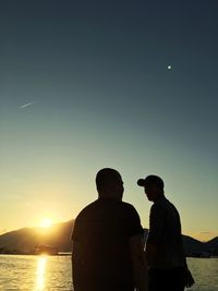 Rear view of silhouette friends against sky during sunset