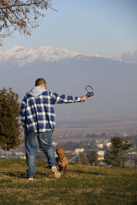 Full length of man playing with dog while standing on field at public park