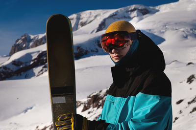 Guy holding a pair of skis and posing on a snowy mountain in a ski resort