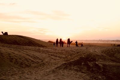 People walking on sand dune in desert against sky