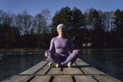 Full length of woman meditating while sitting on pier
