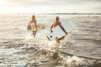 Shirtless men with surfboards walking in sea