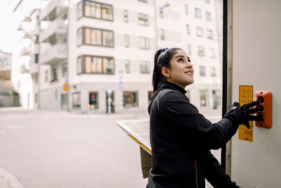 Smiling young delivery woman pressing push buttons on truck in city