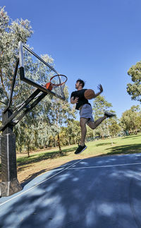 Low angle view of man putting ball in basketball hoop against clear sky