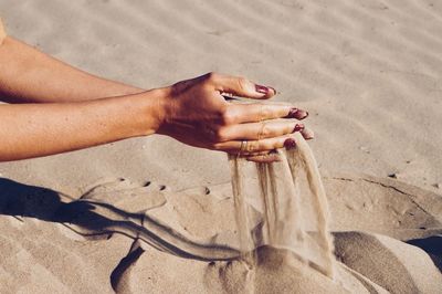 Cropped hands of woman spilling sand at beach